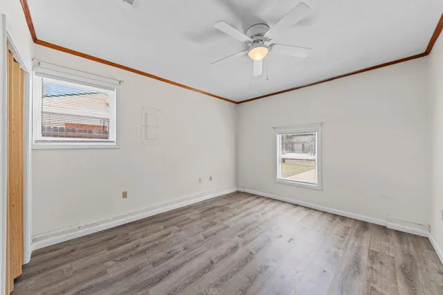 an empty room with wooden floor chandelier fan and windows