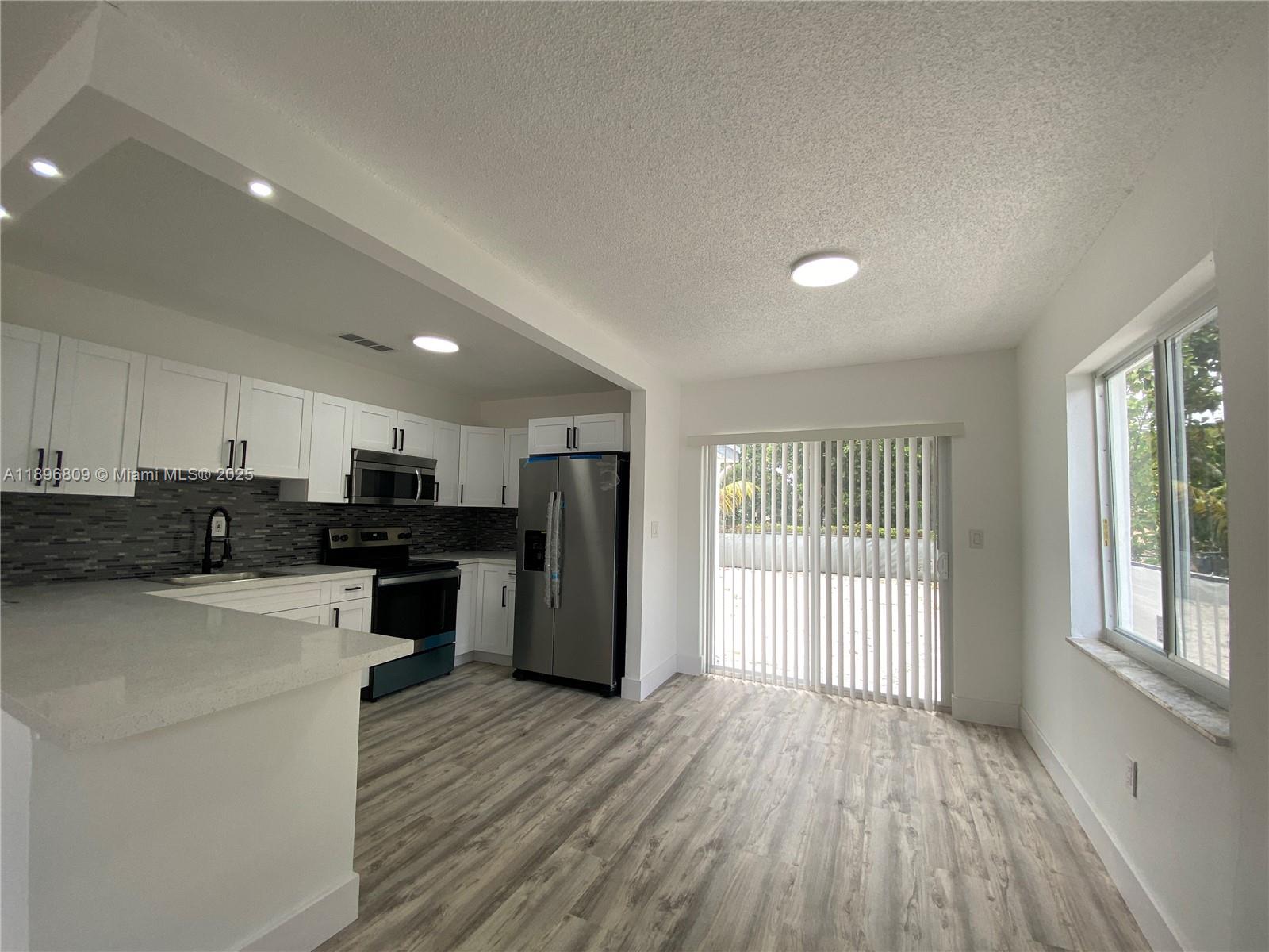 46 Northwest 44th Street, Unit 46 Miami, FL 33127 - Photo 14 of 16 a kitchen with stainless steel appliances kitchen island wooden floors and refrigerator