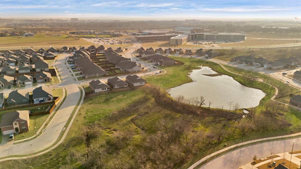 3204 Renaissance Drive Denton, TX 76207 - Photo 4 of 25 Neighborhood with a central pond feature, surrounded by residential properties, streets, and an institutional building in the background