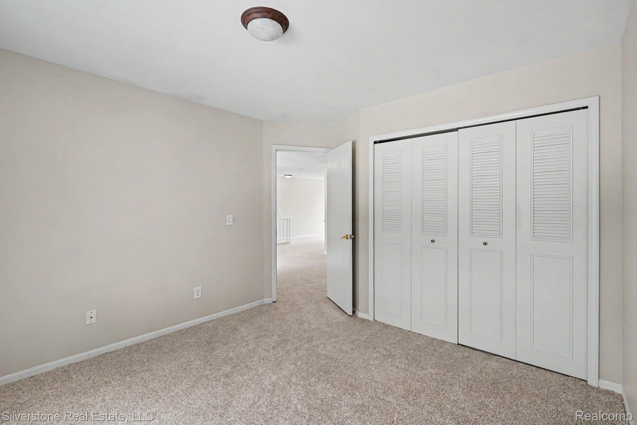 1502 Meadowside Drive Rochester, MI 48307 - Photo 15 of 27 Bedroom featuring light neutral walls, textured carpeting, white bi-fold louvered closet doors, and a ceiling-mounted light fixture