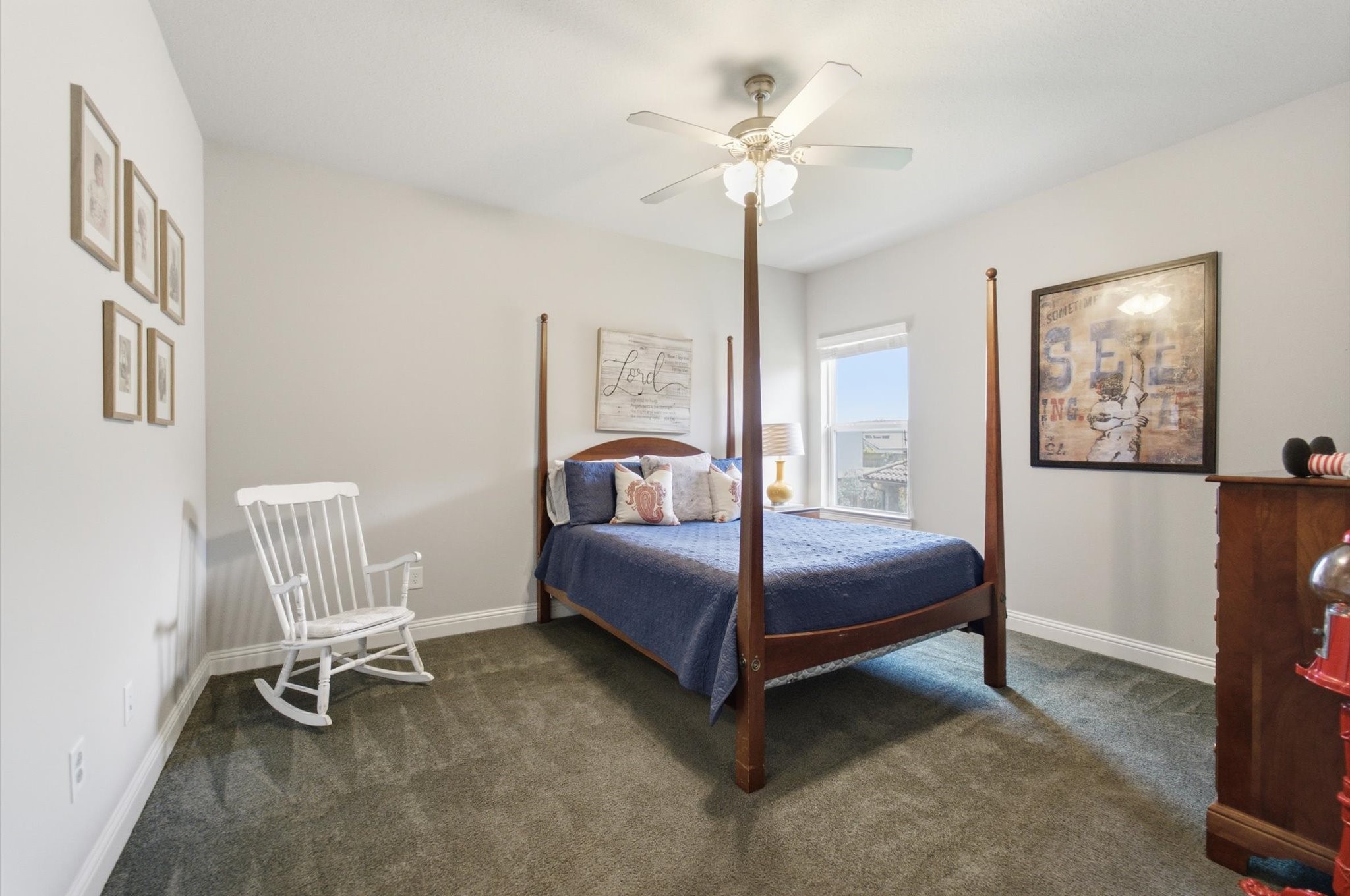 23722 Thortons Park Lane Spring, TX 77389 - Photo 40 of 48 This cozy bedroom features a four-poster bed, a ceiling fan, and ample natural light from a large window. The neutral walls are complemented by tasteful decor, including framed art and a white rocking chair, creating a welcoming atmosphere.