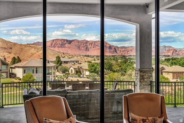 2608 Canyon Ridge Drive St. George, UT 84770 - Photo 12 of 86 Expansive sliding glass doors open to an outdoor living area with a stone pillar and black metal railing, featuring distant red rock formations and verdant landscape