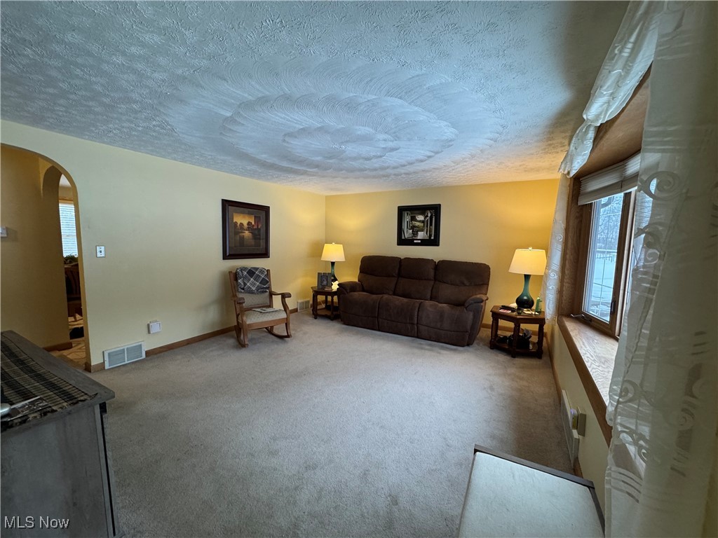 Carpeted living area with arched walkways and a textured ceiling