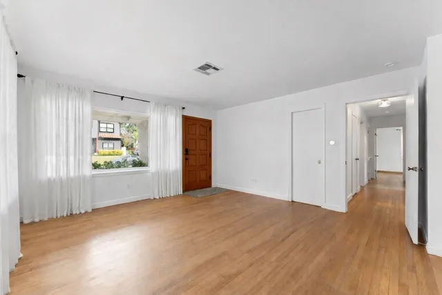 a view of an empty room with wooden floor and a window
