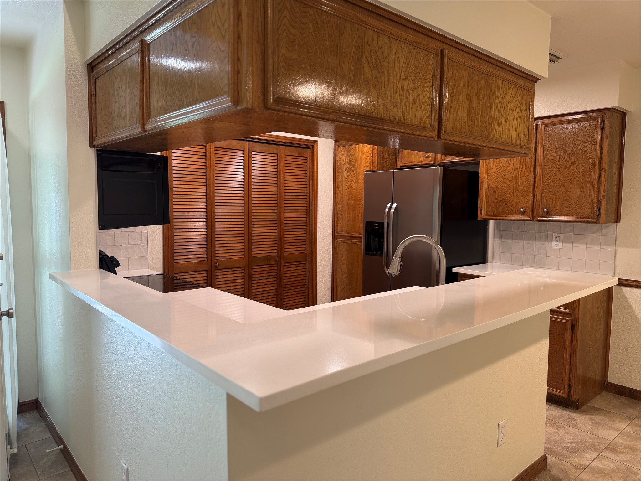 349 Fantail Loop, Unit B Austin, TX 78734 - Photo 2 of 9 Kitchen featuring a white countertop with a built-in sink and a curved faucet, stainless steel refrigerator, wood cabinetry, and a tile backsplash