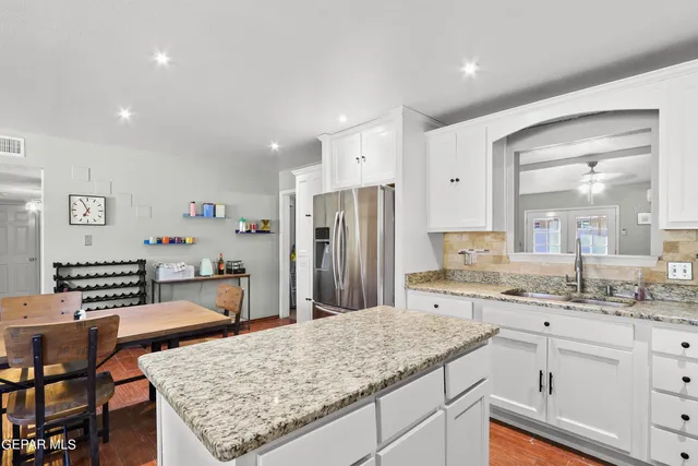 a kitchen with stainless steel appliances granite countertop a dining table chairs refrigerator and sink