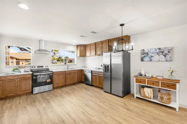 a kitchen with stainless steel appliances granite countertop a refrigerator a stove top oven a sink dishwasher and wooden cabinets with wooden floor
