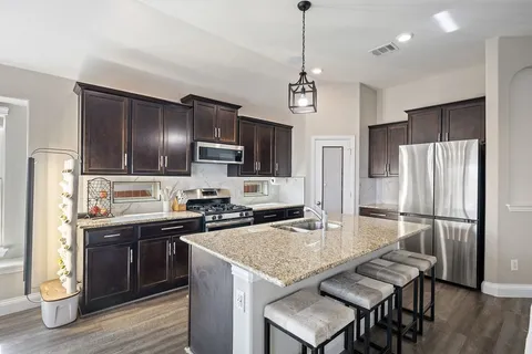 a kitchen with stainless steel appliances granite countertop a sink a stove a refrigerator cabinets and chairs