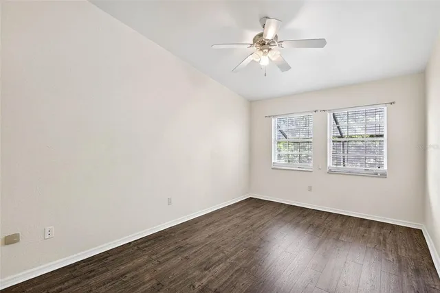 an empty room with wooden floor chandelier fan and windows