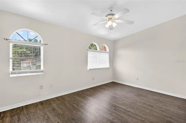 an empty room with wooden floor chandelier fan and windows