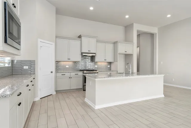 a large kitchen with granite countertop a sink a stove a refrigerator and white cabinets