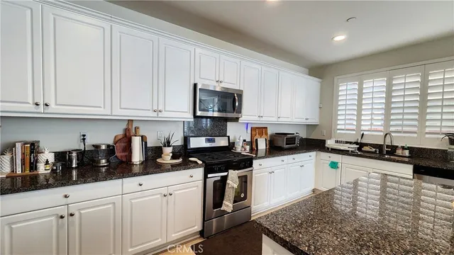 a kitchen with granite countertop a sink a stove top oven a counter space and cabinets