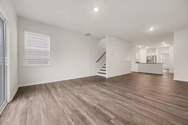 a view of empty room with wooden floor and kitchen