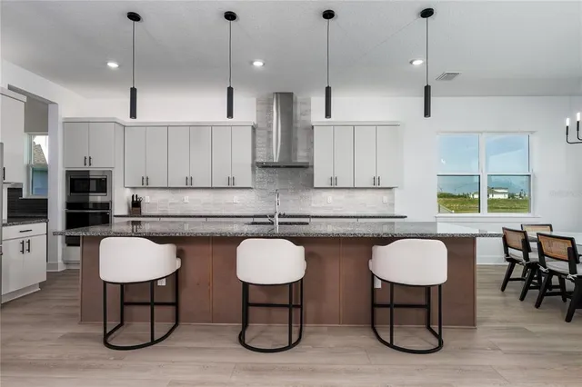 a kitchen with stainless steel appliances granite countertop a sink a stove a refrigerator cabinets and chairs