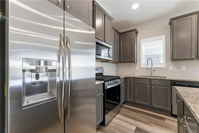 a kitchen with stainless steel appliances granite countertop a refrigerator a stove and a sink with wooden floor