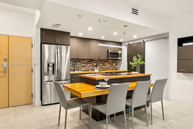 a kitchen with stainless steel appliances granite countertop a dining table chairs refrigerator and sink