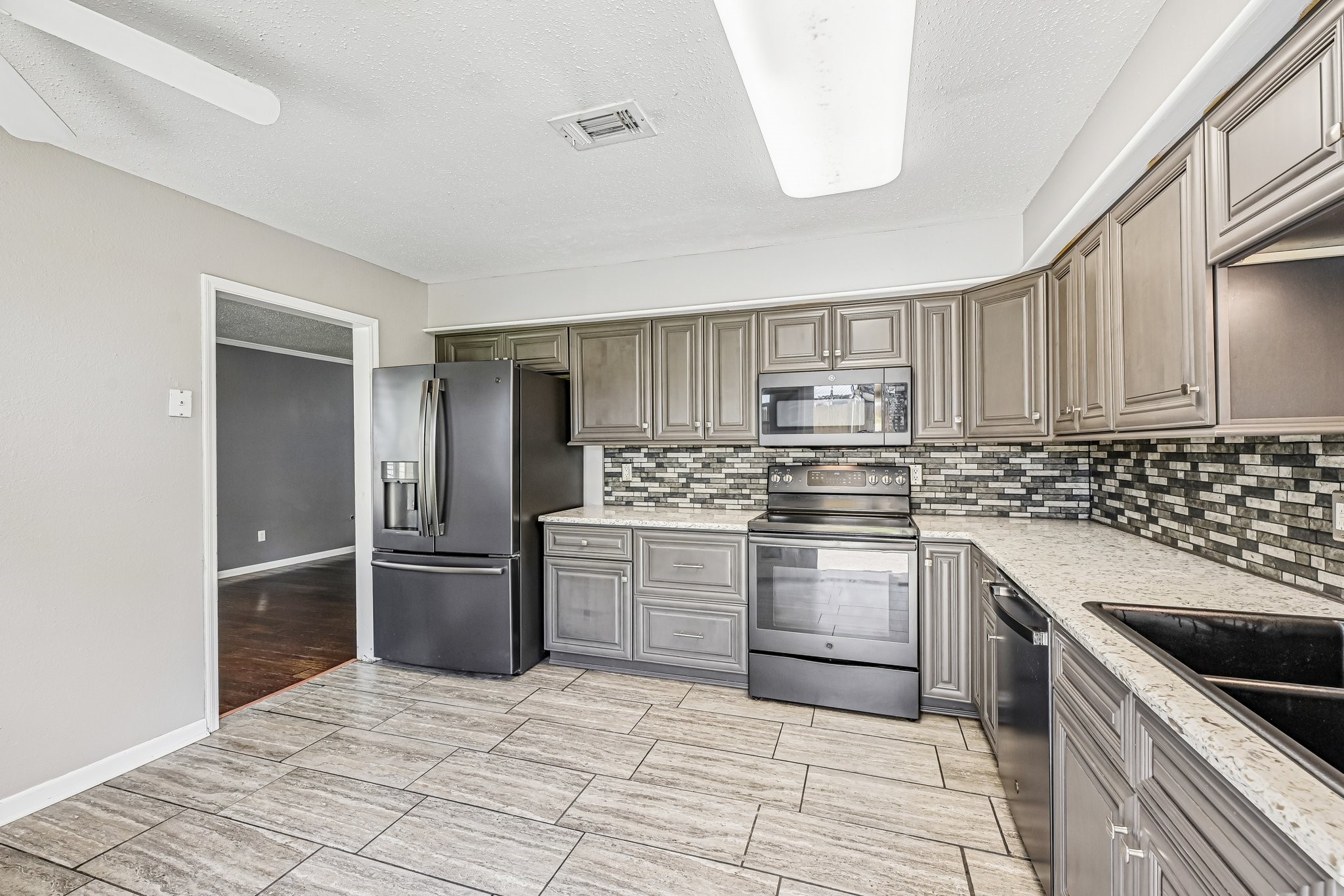 8 Arlington Street Conroe, TX 77301 - Photo 19 of 37 This modern kitchen features sleek gray cabinetry, a stylish tile backsplash, and black appliances. The space is enhanced by ample countertop area and a ceiling fan for comfort.