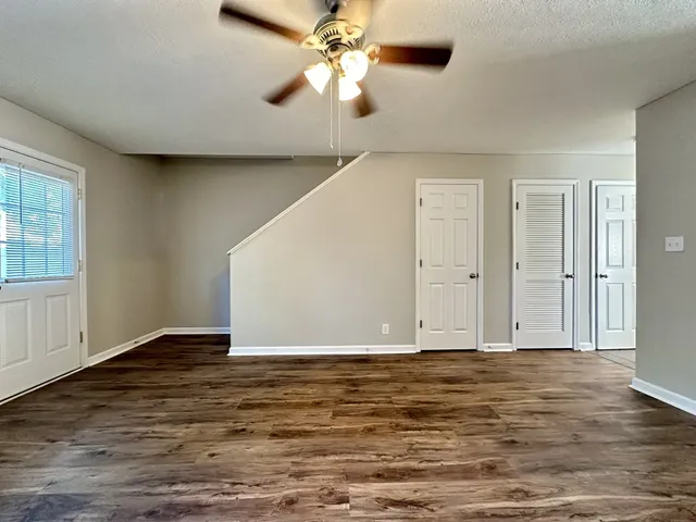 a view of an empty room with wooden floor and a ceiling fan