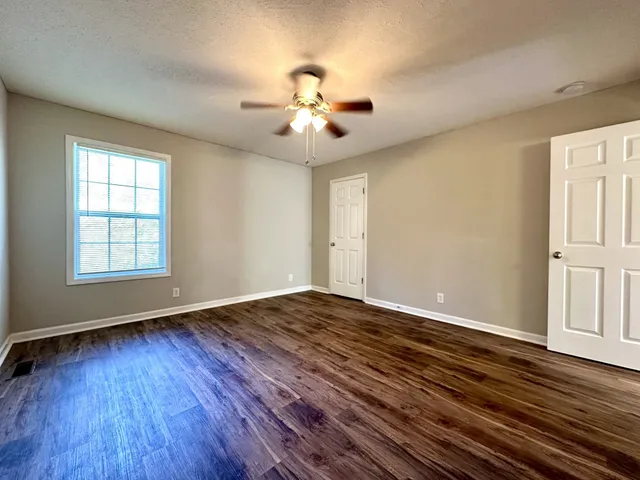 an empty room with wooden floor chandelier fan and windows