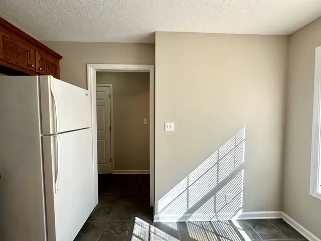 a view of a refrigerator in kitchen and an empty room