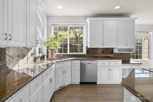 a kitchen with stainless steel appliances granite countertop white cabinets sink and window