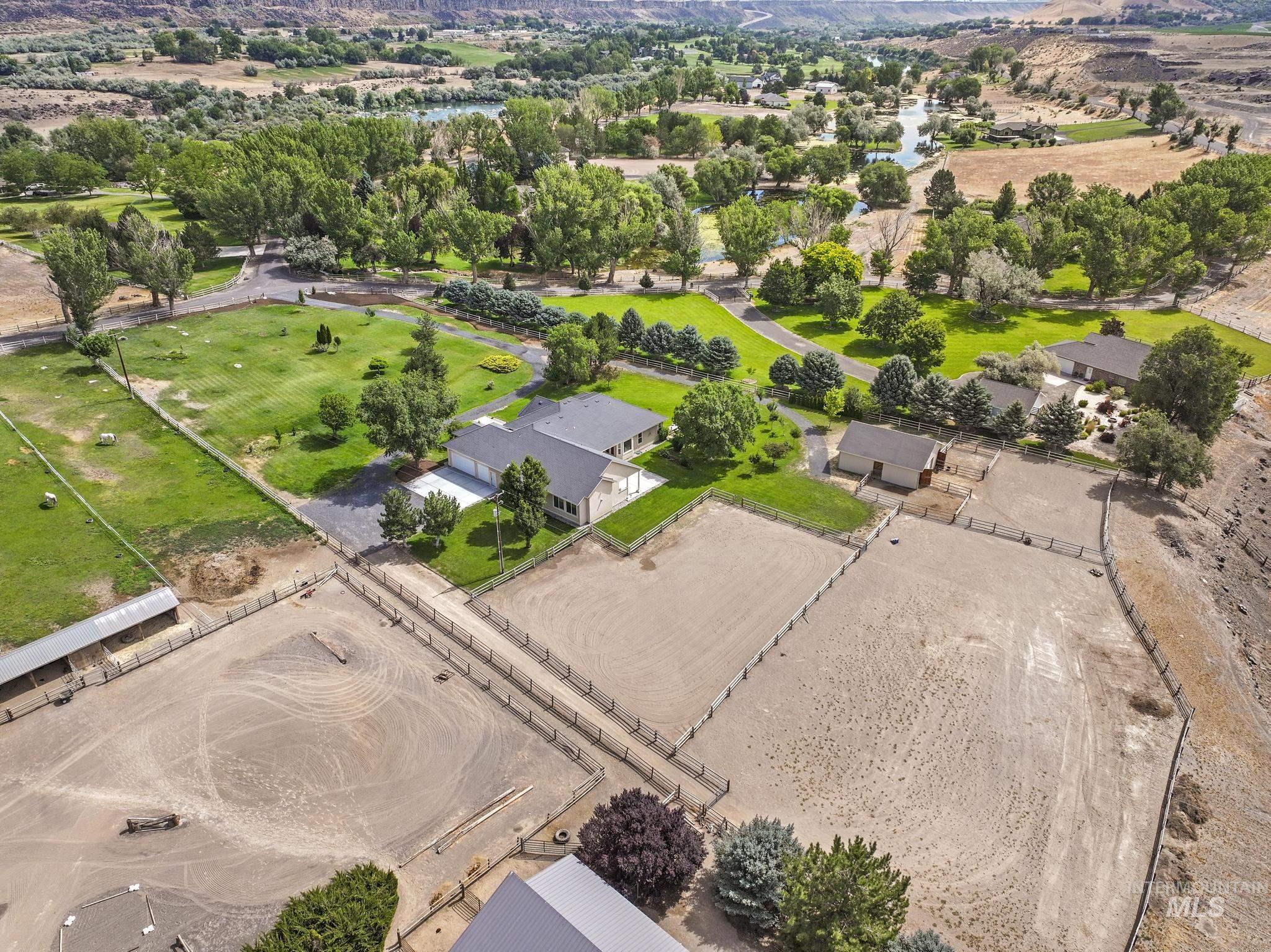 1301 Kanaka Rapids Road Buhl, ID 83316 - Photo 3 of 50 Expansive property featuring multiple fenced equestrian arenas, a main residence with an attached garage, additional outbuildings, and extensive green spaces with mature trees