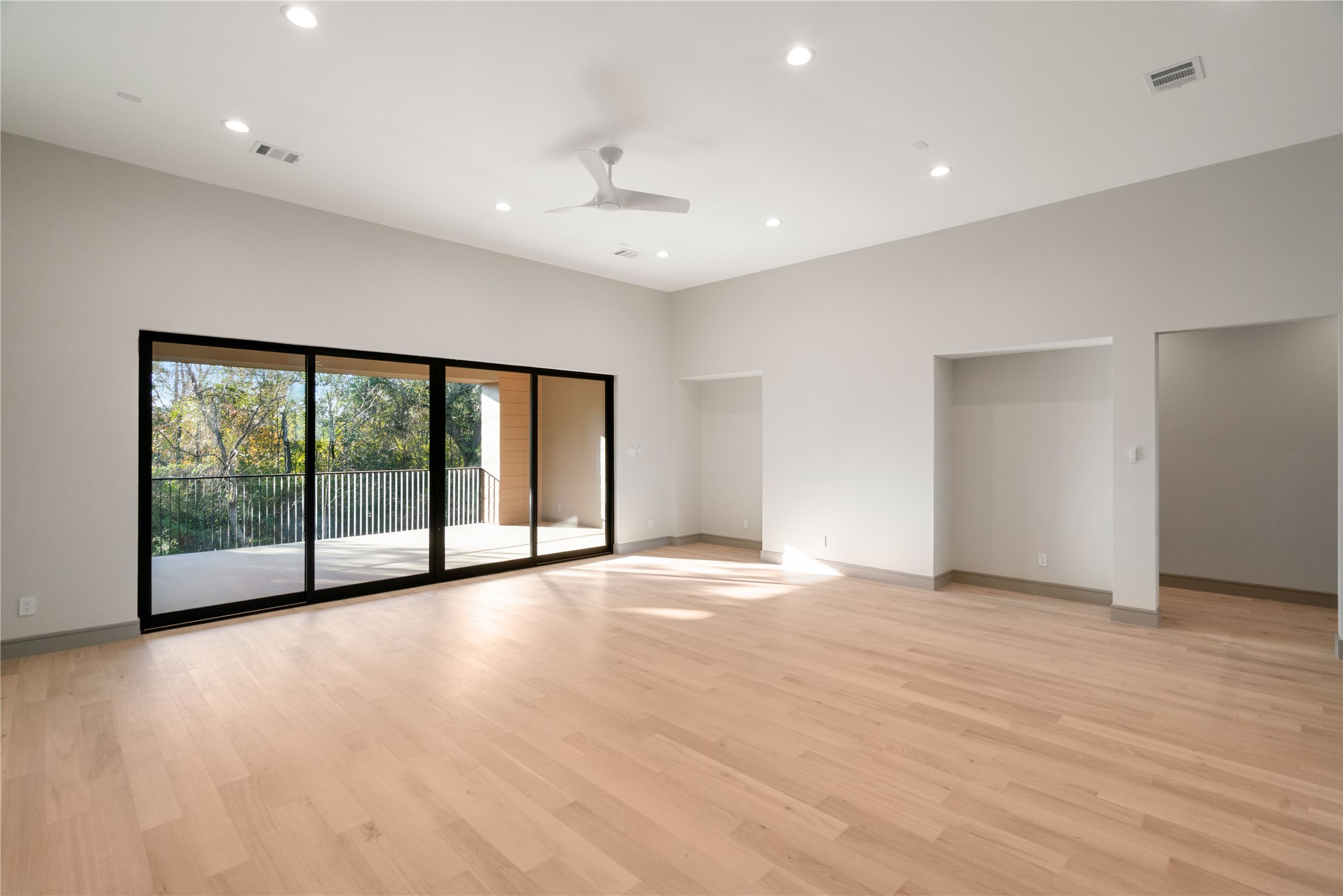 47 Pronghorn Place Spring, TX 77389 - Photo 21 of 44 Spacious and bright living area with light wood flooring and recessed lighting. Large glass sliding doors open to a balcony with a scenic view of trees, providing abundant natural light and a seamless indoor-outdoor flow.