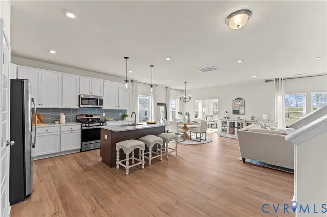 a kitchen with a refrigerator a stove top oven a sink dishwasher a dining table and chairs with wooden floor