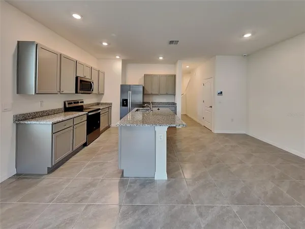 a large kitchen with stainless steel appliances granite countertop a stove a sink a refrigerator a microwave and white cabinets