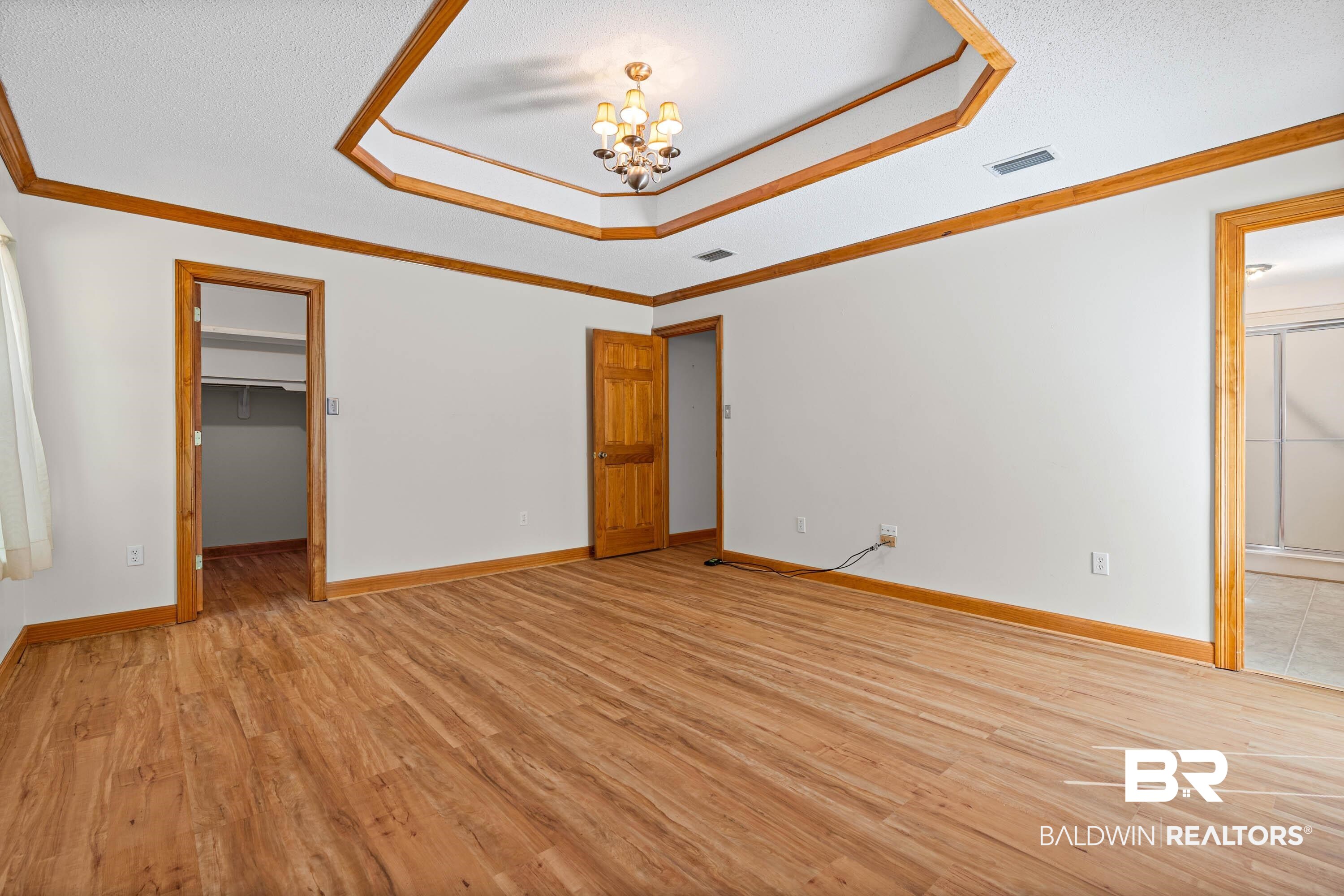 10140 Lakeview Road Bay Minette, AL 36507 - Photo 15 of 35 Unfurnished bedroom with light wood-type flooring, a walk in closet, hanging lights, a textured ceiling, and ornamental molding