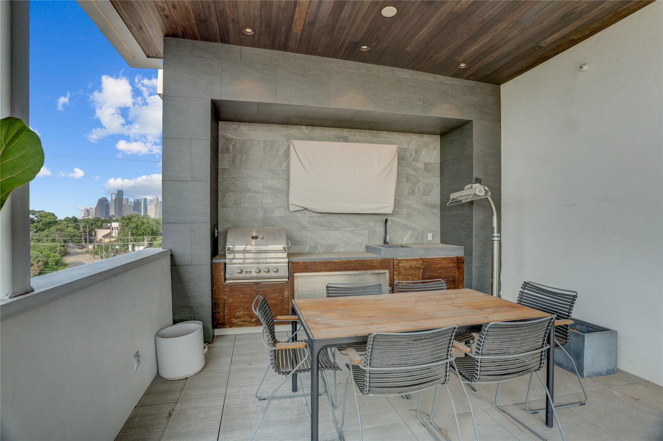 1807 Indiana Street Houston, TX 77006 - Photo 32 of 35 Rooftop Summer Kitchen: Close-up of the covered outdoor kitchen area, highlighting the built-in stainless steel gas grill, prep sink, stone-clad accent alcove, warm wood-paneled ceiling, and clear views of the Downtown Houston skyline.