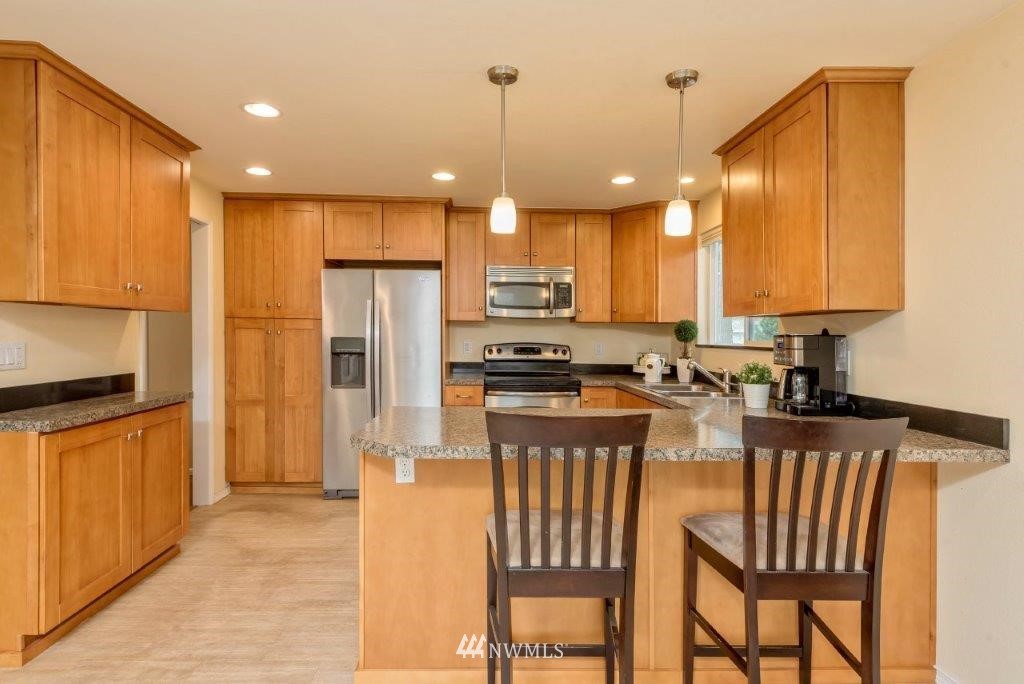 12525 Southeast 99th Street Renton, WA 98056 - Photo 10 of 33 a kitchen with stainless steel appliances granite countertop a refrigerator a stove a sink a dining table and chairs