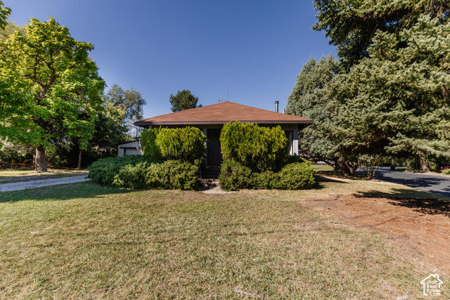 3959 Main Street Logan, UT 84321 - Photo 29 of 35 Single-story residence featuring a brown shingled roof, mature evergreen trees, expansive front lawn, and a gravel driveway