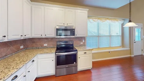 a kitchen with granite countertop a stove a sink and a white cabinets