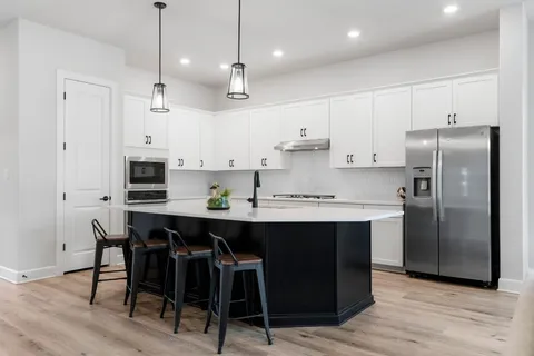 a kitchen with stainless steel appliances granite countertop a table chairs stove and white cabinets