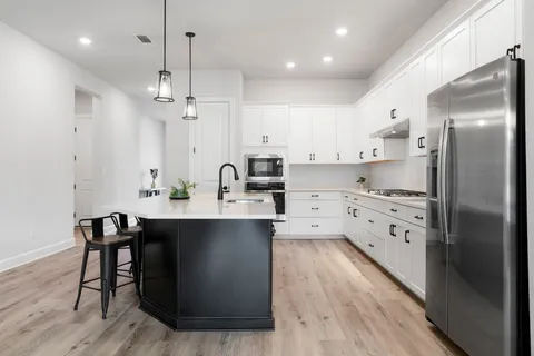 a kitchen with stainless steel appliances granite countertop a sink a stove a refrigerator and white cabinets with wooden floor