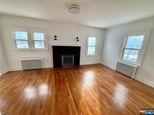 an empty room with wooden floor fireplace and windows