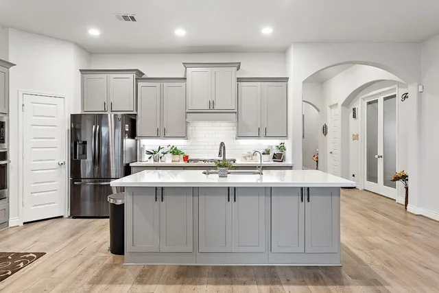 a kitchen with stainless steel appliances granite countertop a sink a stove a refrigerator and island with wooden floor