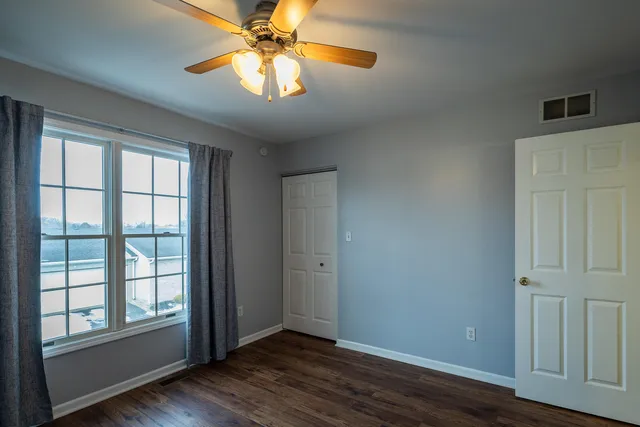 an empty room with wooden floor chandelier fan and windows