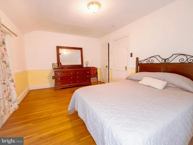 a bedroom with a bed and dresser with wooden floor