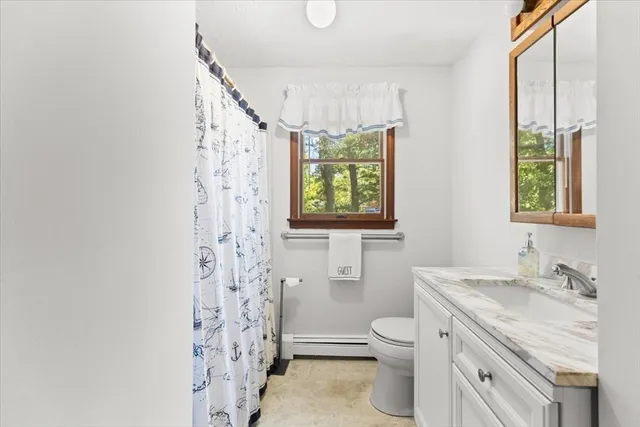 a bathroom with a granite countertop toilet a sink a mirror a window and a shower