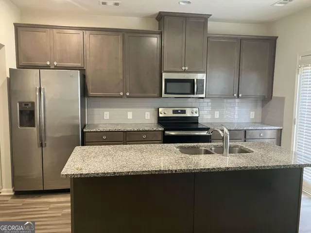 a kitchen with granite countertop a refrigerator a sink and wooden cabinets
