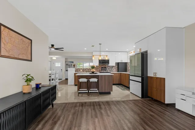 a kitchen with stainless steel appliances kitchen island granite countertop a refrigerator a sink dishwasher a dining table and chairs with wooden floor