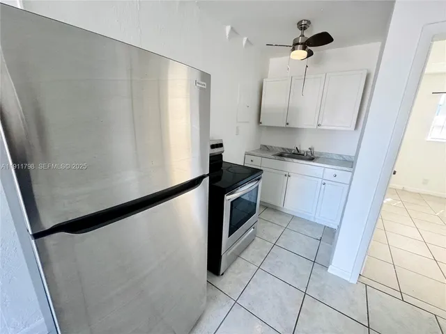 a kitchen with granite countertop a refrigerator a sink and white cabinets