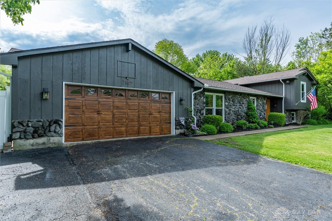 2165 Stewart Road Xenia, OH 45385 - Photo 59 of 59 This charming home features a wooden garage door and stone facade, nestled within a lush green setting.