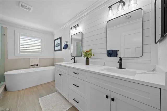 a spacious bathroom with double vanity a mirror a bathtub and window