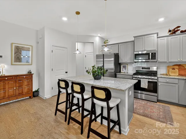 a kitchen with stainless steel appliances kitchen island granite countertop a table chairs sink and cabinets