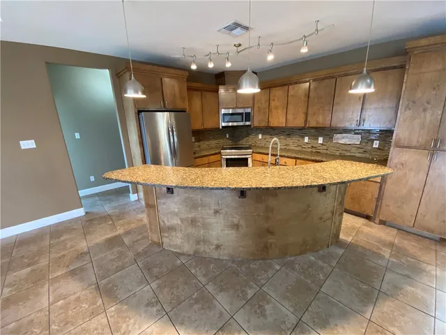 a large kitchen with stainless steel appliances kitchen island granite countertop a refrigerator a sink and a counter top