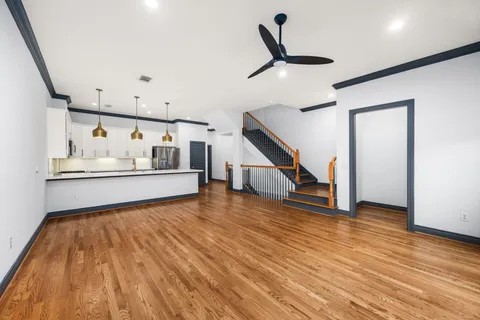 a view of an empty room with wooden floor and fan