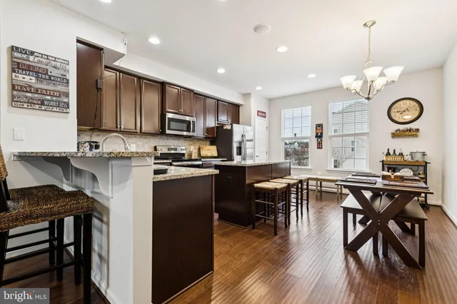 a kitchen with stainless steel appliances granite countertop a stove top oven a sink a dining table and chairs with wooden floor